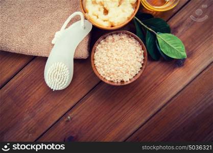 beauty, spa, body care, natural cosmetics and bath concept - close up of himalayan pink salt with brush and towel on wooden table. close up of himalayan salt with brush and towel