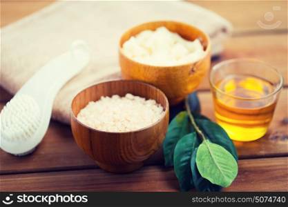 beauty, spa, body care, natural cosmetics and bath concept - close up of himalayan pink salt and body scrub with brush on wooden table. close up of himalayan pink salt and bath stuff
