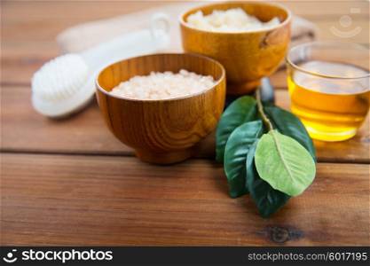 beauty, spa, body care, natural cosmetics and bath concept - close up of himalayan pink salt and body scrub with brush on wooden table