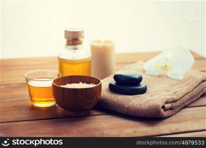 beauty, spa, body care, natural cosmetics and concept - close up of pink salt with massage oil and bath towel on wooden table. close up of salt, massage oil and bath stuff