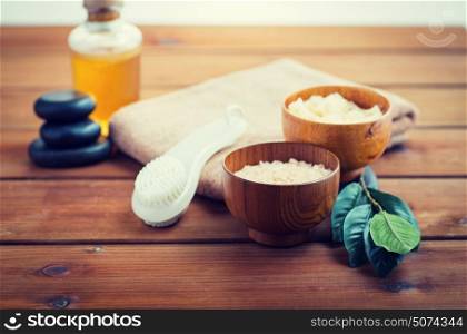 beauty, spa, body care, natural cosmetics and concept - close up of pink salt with massage oil and bath towel on wooden table. close up of salt, massage oil and bath stuff