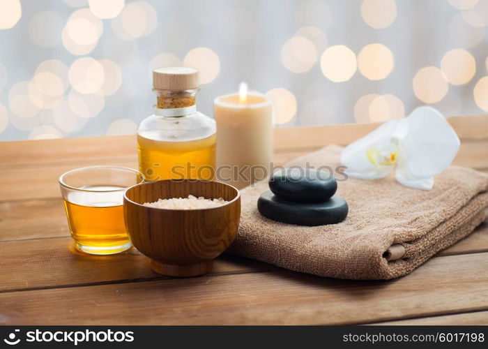 beauty, spa, body care, natural cosmetics and concept - close up of pink salt with massage oil and bath towel on wooden table