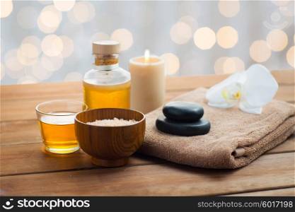 beauty, spa, body care, natural cosmetics and concept - close up of pink salt with massage oil and bath towel on wooden table