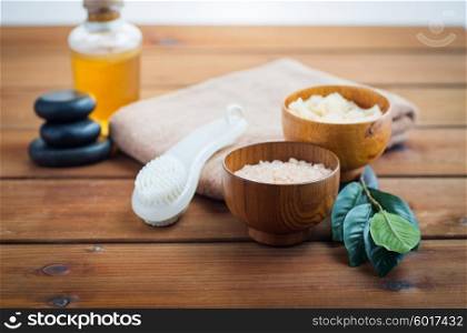 beauty, spa, body care, natural cosmetics and concept - close up of pink salt with massage oil and bath towel on wooden table