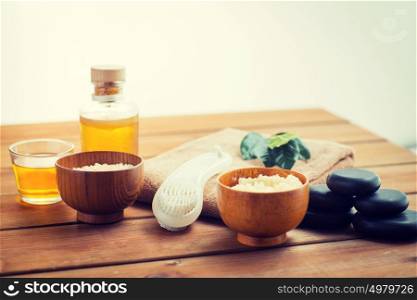 beauty, spa, body care, natural cosmetics and massage concept - close up of body scrub with brush on wooden table. close up of scrub, massage oil and bath stuff