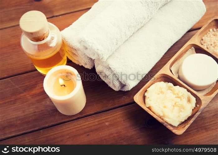 beauty, spa, body care, natural cosmetics and wellness concept - close up of soap with candle and bath towels on wooden table. close up of natural cosmetics and bath towels