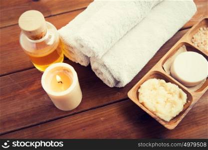 beauty, spa, body care, natural cosmetics and wellness concept - close up of soap with candle and bath towels on wooden table. close up of natural cosmetics and bath towels
