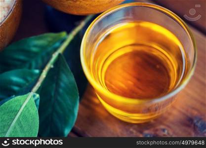 beauty, spa, body care, natural cosmetics and wellness concept - close up of honey in glass cup with leaves on wooden table. close up of honey in glass with leaves on wood