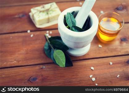 beauty, spa, body care, natural cosmetics and wellness concept - close up of mortar and pestle with leaves with leaves on wooden table. close up of mortar with leaves on wood
