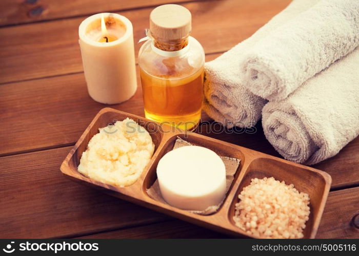 beauty, spa, body care, natural cosmetics and wellness concept - close up of soap with candle and bath towels on wooden table. close up of natural cosmetics and bath towels