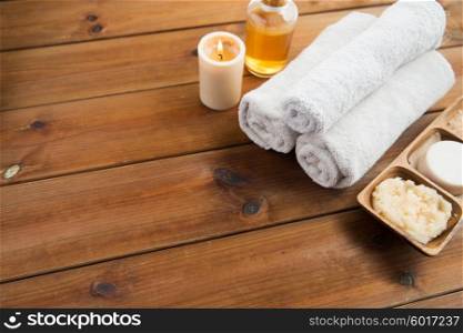 beauty, spa, body care, natural cosmetics and wellness concept - close up of soap with candle and bath towels on wooden table