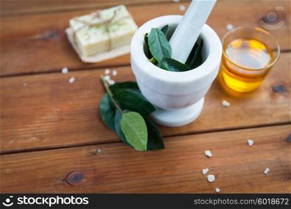 beauty, spa, body care, natural cosmetics and wellness concept - close up of mortar and pestle with leaves with leaves on wooden table