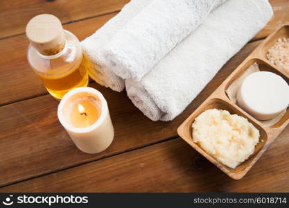 beauty, spa, body care, natural cosmetics and wellness concept - close up of soap with candle and bath towels on wooden table