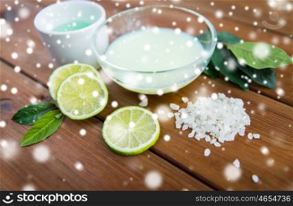 beauty, spa, bodycare and natural cosmetics concept - bowls with citrus body lotion, cream and sea salt on wooden table over snow