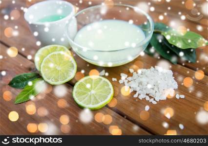 beauty, spa, bodycare and natural cosmetics concept - bowls with citrus body lotion, cream and sea salt on wood over lights and snow