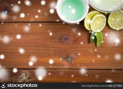 beauty, spa, bodycare and natural cosmetics concept - f bowls with citrus body lotion, cream and limes on wooden table over snow