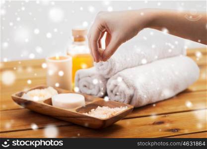 beauty, spa, bodycare and natural cosmetics concept - hand pouring himalayan salt in wooden bowl with soap, scrub and bath towels on table over snow