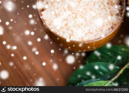 beauty, spa, bodycare, bath and natural cosmetics concept - close up of himalayan pink salt in wooden bowl with leaves over snow
