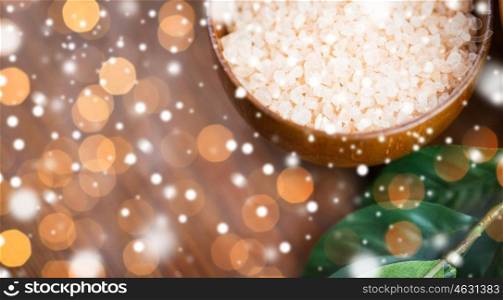 beauty, spa, bodycare, bath and natural cosmetics concept - close up of himalayan pink salt in wooden bowl with leaves over lights and snow