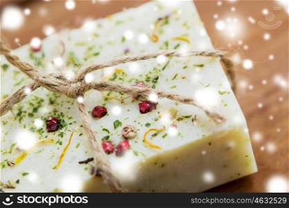 beauty, spa, bodycare, bath and natural cosmetics concept - close up of handmade soap bars on wooden table over snow