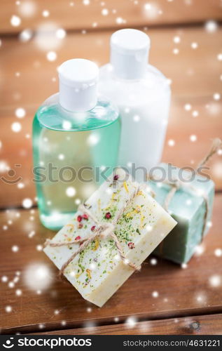 beauty, spa, bodycare, bath and natural cosmetics concept - handmade soap bars and lotion bottles on wooden table over snow