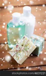 beauty, spa, bodycare, bath and natural cosmetics concept - handmade soap bars and lotion bottles on wooden table over snow