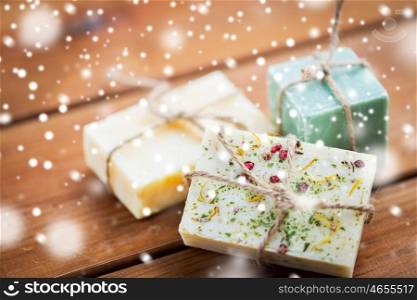 beauty, spa, bodycare, bath and natural cosmetics concept -handmade soap bars on wooden table over snow