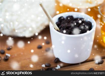 beauty, spa, bodycare, bath and natural cosmetics concept - homemade coffee scrub in cup on wooden table over snow