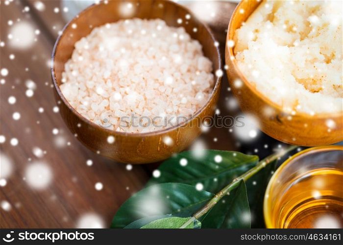 beauty, spa, bodycare, natural cosmetics and and wellness concept - close up of himalayan pink salt and body scrub with leaves on wooden table over snow