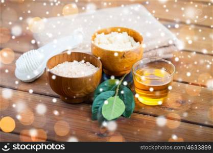 beauty, spa, bodycare, natural cosmetics and bath concept - close up of himalayan pink salt and body scrub with brush and towel on wooden table over lights and snow