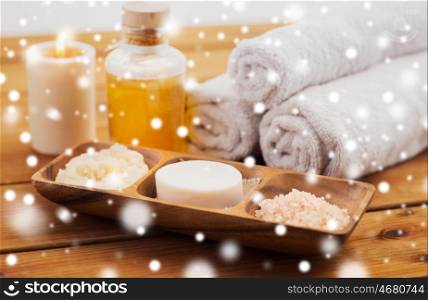 beauty, spa, bodycare, natural cosmetics and bath concept - soap with himalayan salt with scrub in wooden bowl and massage oil on table over snow