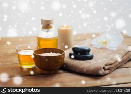 beauty, spa, bodycare, natural cosmetics and concept - himalayan pink salt with massage oil and bath towel on wooden table over snow