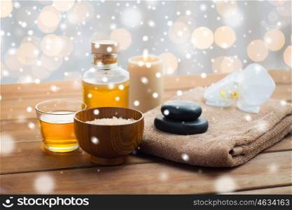 beauty, spa, bodycare, natural cosmetics and concept - himalayan pink salt with massage oil and bath towel on wooden table over lights and snow