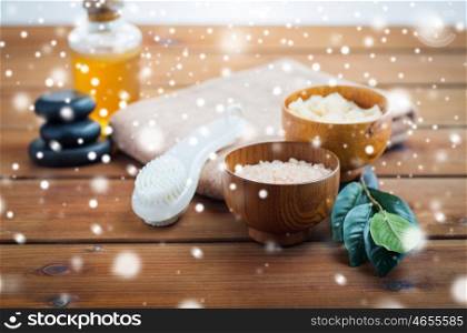 beauty, spa, bodycare, natural cosmetics and concept - himalayan pink salt with massage brush and bath towel on wooden table over snow. himalayan pink salt, massage brush and bath towel