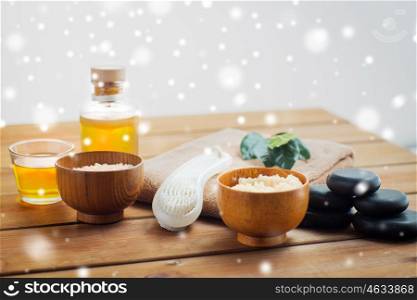 beauty, spa, bodycare, natural cosmetics and massage concept - body scrub with brush and massage oil on wooden table over snow
