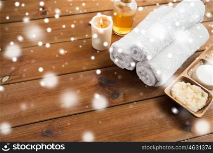 beauty, spa, bodycare, natural cosmetics and wellness concept - bath towels with candle and massage oil with body scrub on wooden table over snow