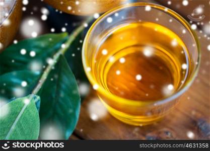 beauty, spa, bodycare, natural cosmetics and wellness concept - close up of honey in glass cup with leaves on wooden table over snow