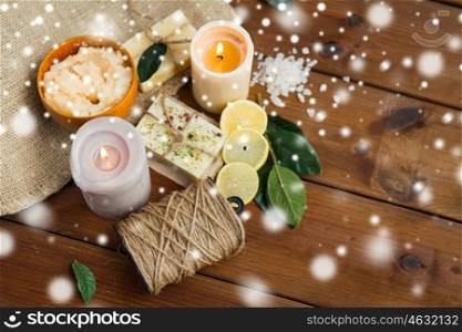 beauty, spa, bodycare, natural cosmetics and wellness concept - handmade soap bars and body scrub with candles on wood over snow