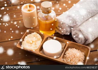 beauty, spa, bodycare, natural cosmetics and wellness concept - soap with candle and bath towels on wooden table over snow