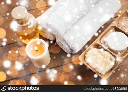 beauty, spa, bodycare, natural cosmetics and wellness concept - soap with candle and bath towels on wooden table over lights and snow