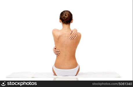 beauty, spa, people and bodycare concept - beautiful topless young woman in white panties sitting on towel from back. beautiful topless young woman on towel from back