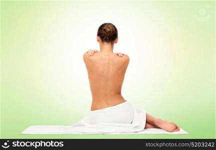 beauty, spa, people and bodycare concept - beautiful young woman in white towel with bare top from back over green background. beautiful young woman in towel with bare back