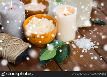 beauty, spa, therapy and natural cosmetics concept - body scrub, salt and candles on wood over snow