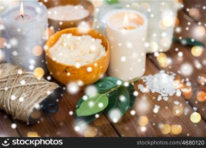 beauty, spa, therapy and natural cosmetics concept - body scrub, salt and candles on wood over lights and snow