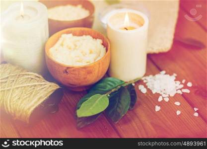 beauty, spa, therapy and natural cosmetics concept - close up of body scrub, salt and candles on wood