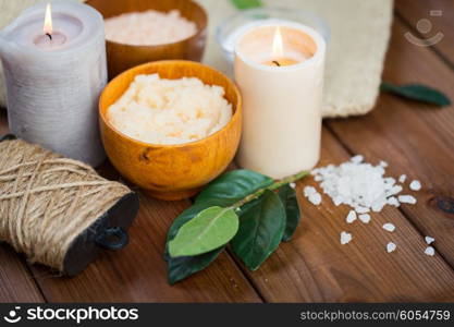 beauty, spa, therapy and natural cosmetics concept - close up of body scrub, salt and candles on wood