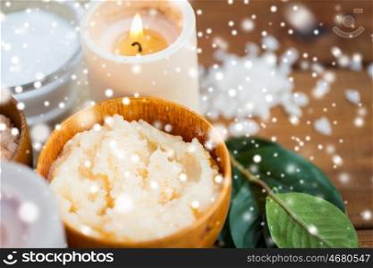 beauty, spa, therapy, natural cosmetics and wellness concept - close up of body scrub and candle on wood over snow