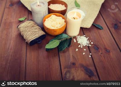 beauty, spa, therapy, natural cosmetics and wellness concept - close up of body scrub with himalayan pink salt and candles on wood. close up of natural body scrub and candles on wood