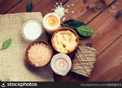 beauty, spa, therapy, natural cosmetics and wellness concept - close up of body scrub with himalayan pink salt and candles on wood. close up of natural body scrub and candles on wood