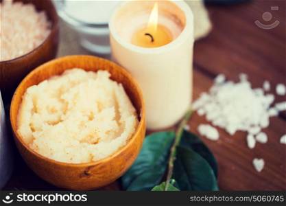 beauty, spa, therapy, natural cosmetics and wellness concept - close up of body scrub and candle on wood. close up of natural body scrub and candle on wood